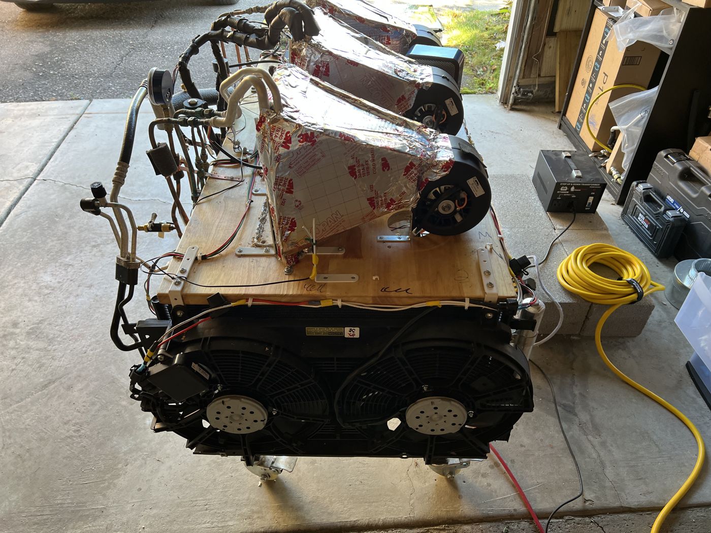 The rebuilt test bench in a garage doorway, with two large fans at the front and three blowers in insulated ducts on top